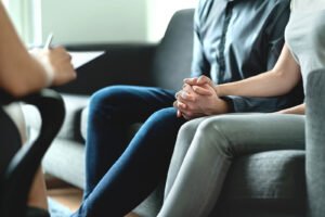 Image of a couple sitting on a couch meeting with a San Diego couples therapist. Couples therapy sessions like this in San Diego can help you feel closer with your partner. Follow the steps in this blog and reach out to a marriage counselor for support