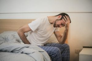 Image of a man sitting on a bed holding his head. Getting more and better sleep is one way to reduce stress. If you are like this man therapy for stress can help. Stop dreading Sunday night and start finding options for stress management.