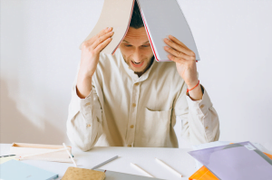 Image of a man covering his head with work papers. Showing the type of situations that stress management can help with. A therapist can help you cope with stress through therapy in San Diego, CA