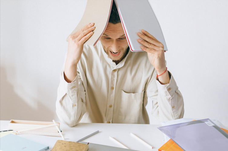 Image of a man covering his head with work papers. Showing the type of situations that stress management can help with. A therapist can help you cope with stress through therapy in San Diego, CA