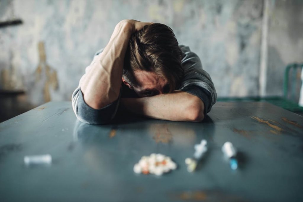 Image of a man fighting to stay in addiction recovery with pills and needles on the table in front of him. Temptations are hard but in addiction treatment you can learn tools that make it easier. There are many skills and tools taught in San Diego addictions counseling that can help you walk away. If you feel like you are in the same position as the man in the photo our addictions counselor can help.