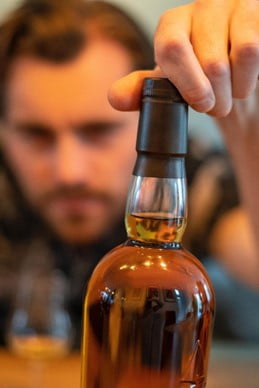 Image of a man grabbing a whiskey bottle. Showing a time when alcohol counseling in San Diego, CA couple help with healing from addiction. You can get support to stop overdrinking with San Diego addictions counseling.