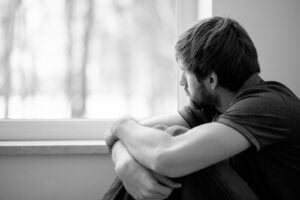 Black and white image of a man looking sadly out a window. Representing the negative impact of painful experiences that trauma therapy and EMDR therapy can help address in San Diego. A trauma therapist can help you overcome the hurt so you can live happily.