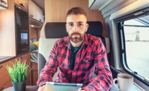 Man in a plaid shirt in a campervan looking directly at the camera, but also on a video call. He appears to be distraught and searching for men's mental health help.