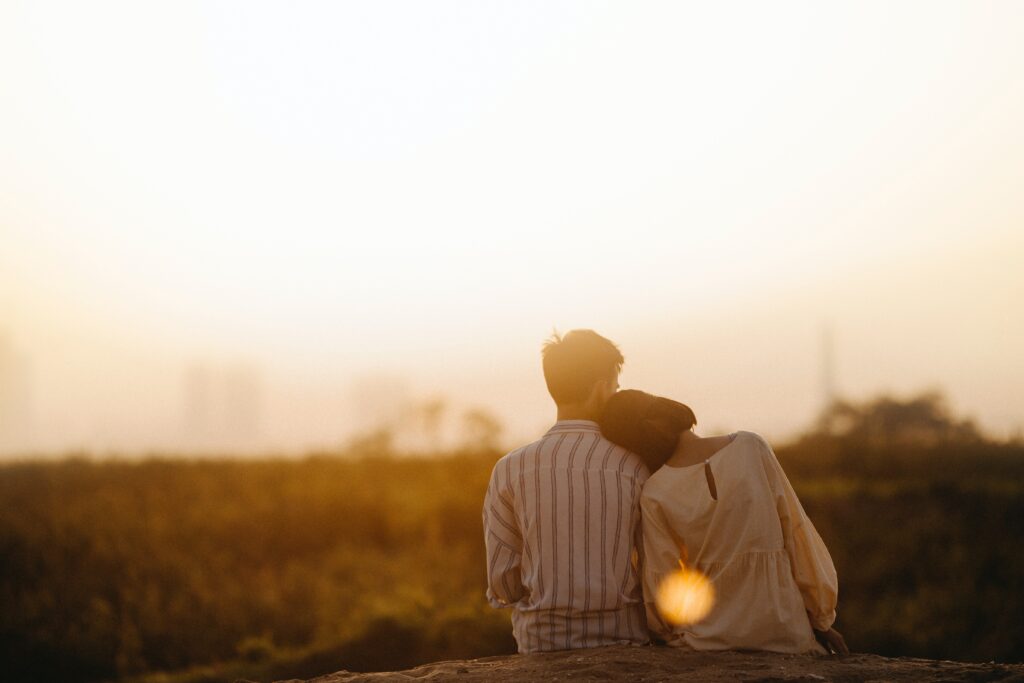 A young and hopeful couple facing a sunset with the woman's head on the man's shoulder taking in a peaceful moment together after utilizing some of the skills they have learned in couples therapy.