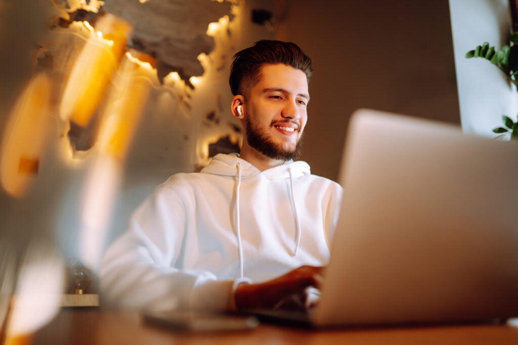 Young man using laptop to simulate participating in online therapy for men in Florida, California or Oregon.