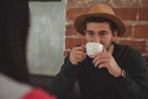 A younger man sips on a cup of coffee while thinking about if he is dating the right person for him.