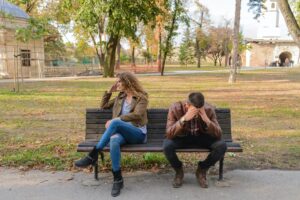 A man and woman sitting on a park bench considering couples therapy, looking defeated and feeling like they are always fighting