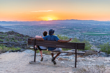 A couple sitting on a park bench with their back to the camera watching the sunset over the horizon for a date night idea in San Diego. Learn more about the support a San Diego couples therpaist can offer support. Learn more about couples therapy in San Diego and other services like online couples therapy in San Diego, CA 