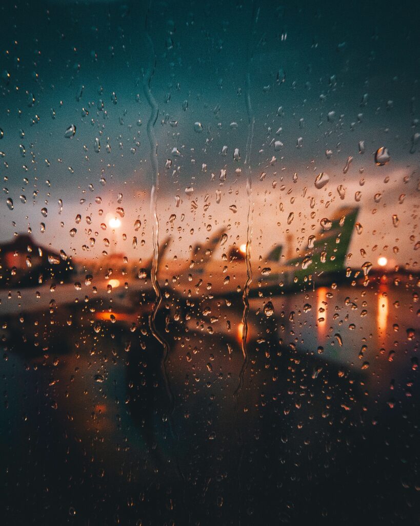 An image of raindrops on a airplane window looking out at the airport during sunrise