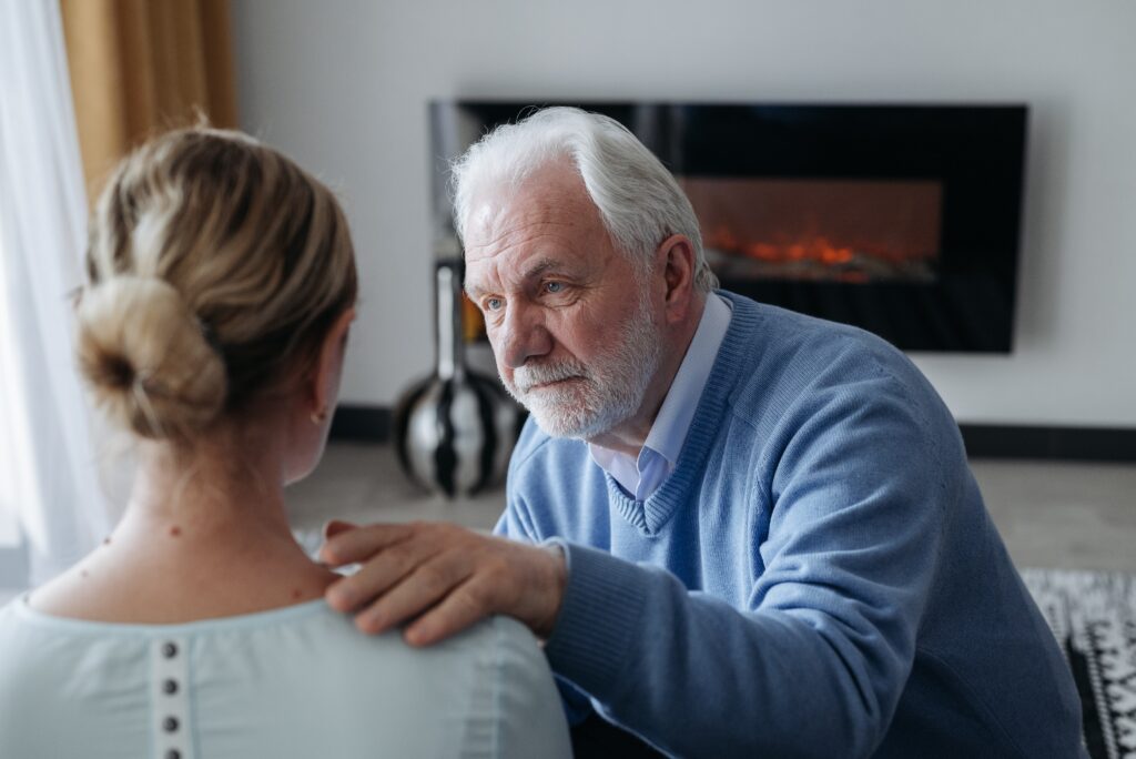 An older couple sitting on a couch in their living room having a deep conversation as they begin the mending process after infidelity has occurred. 