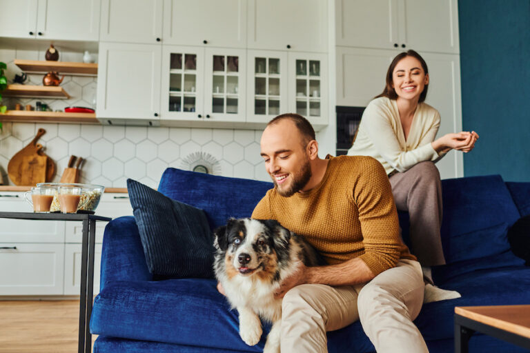 Smiling man petting border collie while sitting near girlfriend on couch; represents someone who feels less stress in his relationships and life in general