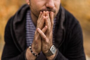 A close-up image of a man with his hands folded in front of his face, conveying the struggle of managing obsessive thinking and intense emotions