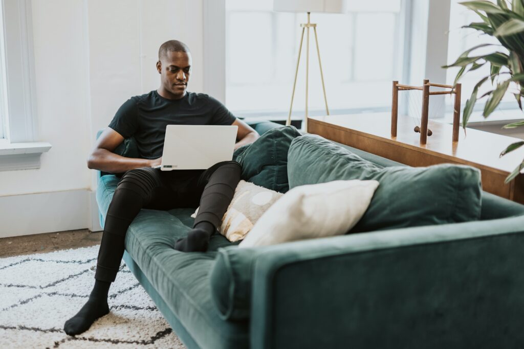 A man sits on a sofa while browsing their laptop. Learn how to connect with an online therapist in California to learn more about online therapy in Oregon and beyond! 