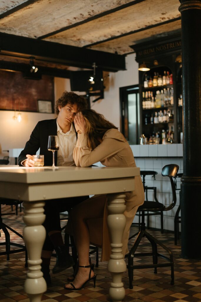 A couple sits together at an empty bar with sad experssions. Learn how a San Diego couples therapist can offer support with couples therapy in San Diego by searching for online couples counseling in California. They can also offer online couples counseling in Portland, OR and more. 