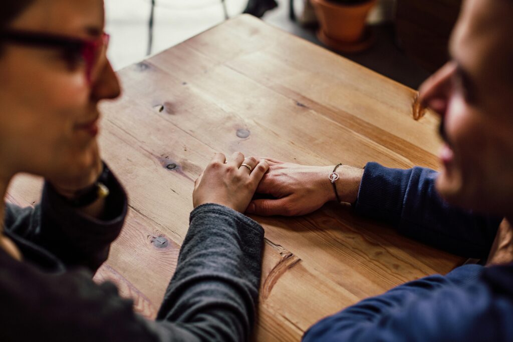 An image of a couple sitting at a table with their hands held representing the partners support for addiction
