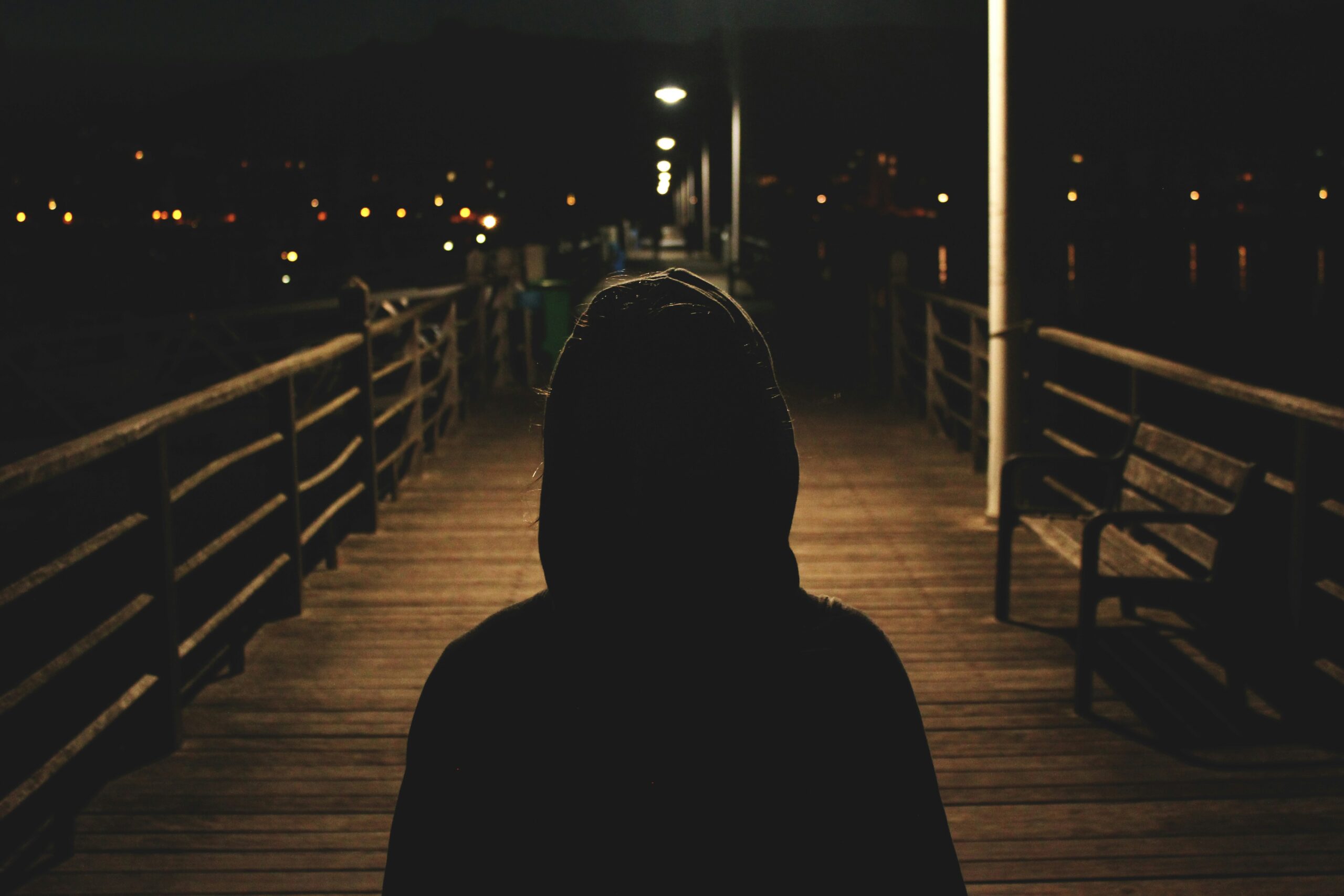 An image of the back of a person walking down a boardwalk in dark clothes at night time representing the state of fear that can lead to irrational thinking without proper help and therapy for men in California.