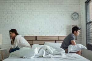 An image of a couple sitting on opposite ends of the bed facing away from each other representing the distance in their relationship during a time where they aren't having sex. My Stress Solutions offers therapy for couples in California experiencing a disconnect in their relationship.