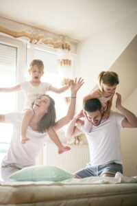 An image of a couple playing with their children in a sunlit bedroom. This image shows the family expressing happiness after couples counseling with Jordan Zipkin in California.