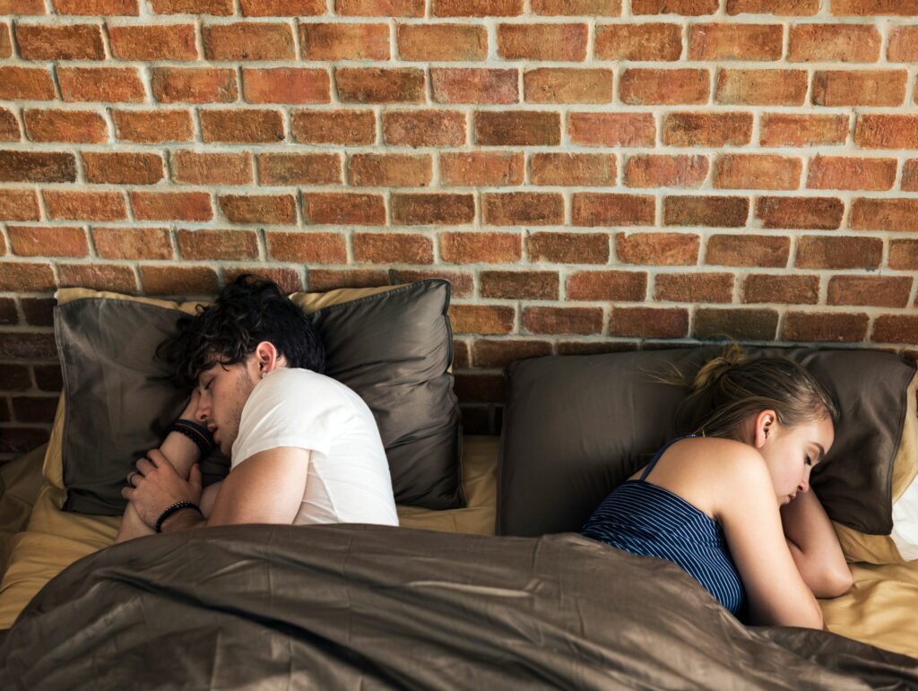 An image of a couple laying in bed with their backs turned toward each other subtly conveys their underlying relationship happiness and stability through the help of therapy in California.