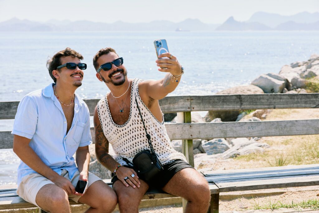 An image of two men smiling and taking a selfie on a bench representing their relationship happiness and stability through the help of couples therapy in California. 