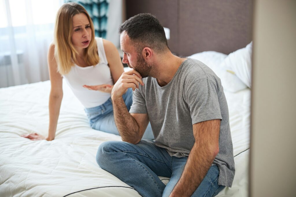 A couple sitting on their bed having an intense discussion, highlighting the struggles of communication in relationships. This represents the common issue of why my partner and I fight and how a relationship therapist might help.