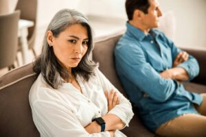 A couple sitting distantly with arms crossed, representing the emotional disconnect and avoidance typical of relationship withdrawal.