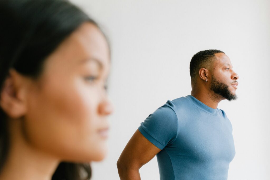 A couple standing apart, both appearing deep in thought and emotionally distant. This image conveys the emotional disconnect that can lead couples to wonder, why my partner and I fight, and seek guidance from a relationship therapist.