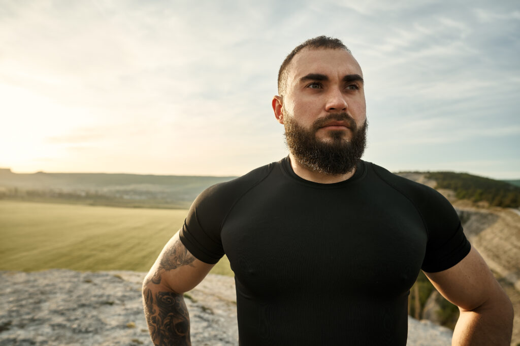 Bearded man standing on a mountain with a serious look, illustrating strength, emotional introspection, and the challenge of overcoming emotional suppression stress.