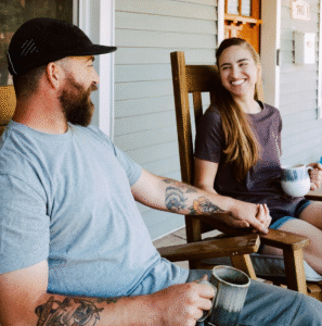 Smiling couple holding hands and coffee mugs on a porch, sharing a moment of connection—showing the positive impact of men’s mental health support.