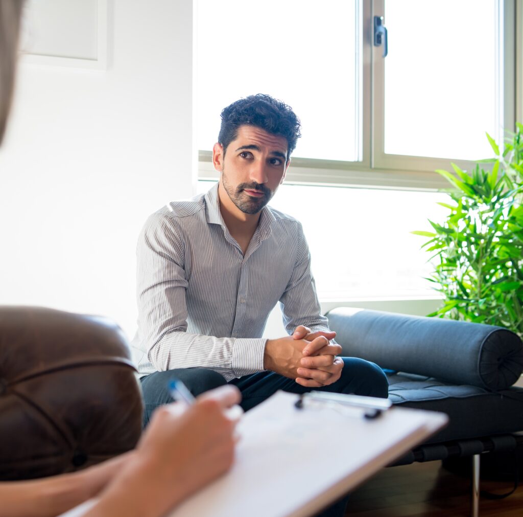 A man sitting in a therapy session, reflecting on his thoughts as he opens up about his mental health. Anxiety therapy for men offers a supportive space to explore and address underlying struggles.