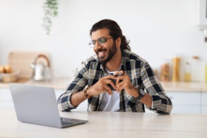 A man smiling during an online therapy session at home, representing therapy for men and the flexibility of online therapy in California as one of the key virtual counseling benefits.