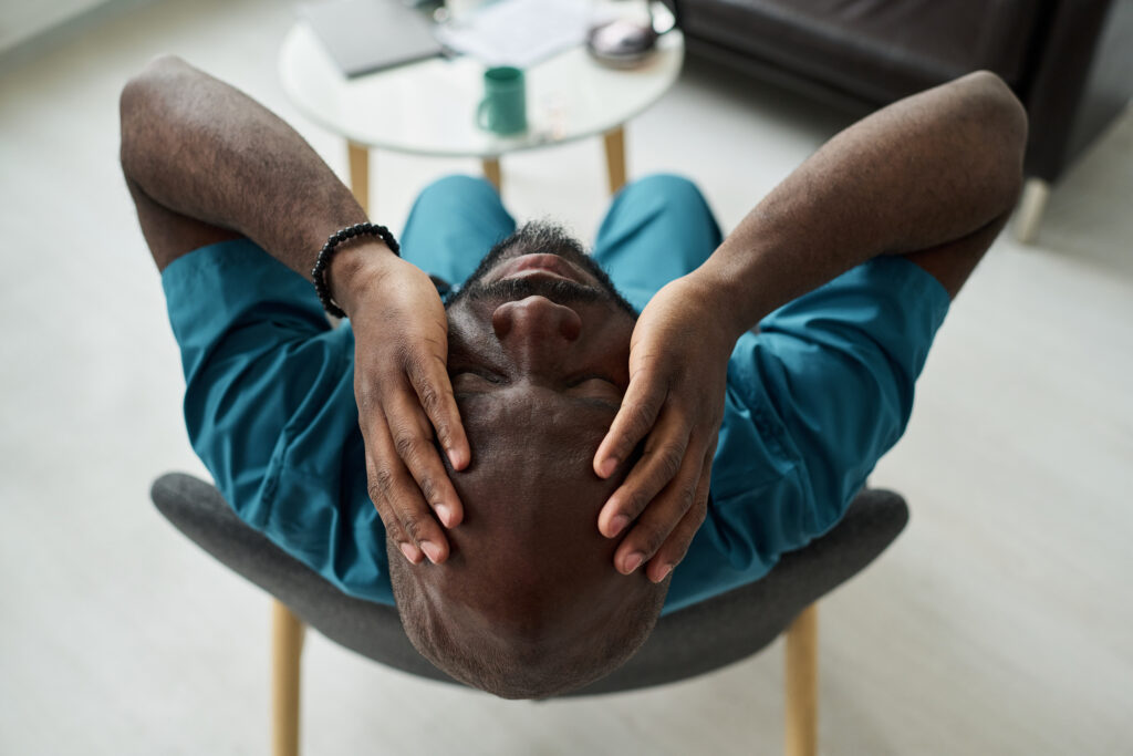 A man sitting back in a chair with hands on his head, showing tension and exhaustion—symbolizing hidden anxiety in men and the importance of men’s mental health support and anxiety therapy in California.