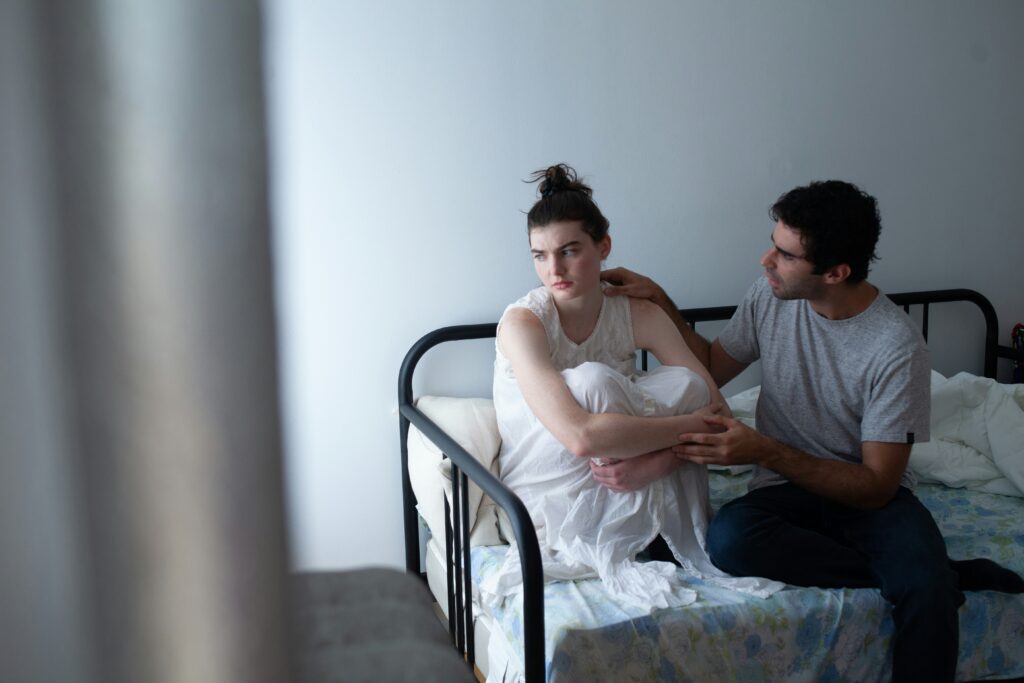 A couple sitting on a bed in a tense moment, with one partner comforting the other—illustrating conflict and the need for relationship repair through learning how to apologize and communicate in couples therapy in California.