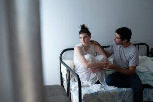 A couple sitting on a bed in a tense moment, with one partner comforting the other—illustrating conflict and the need for relationship repair through learning how to apologize and communicate in couples therapy in California.