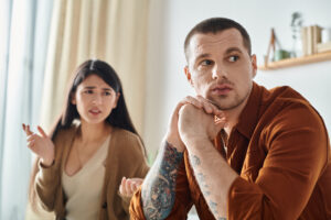 Couple arguing at home, partner looks away while the other asks questions—signs of couples fighting all the time and learning how to fight fair in a relationship.