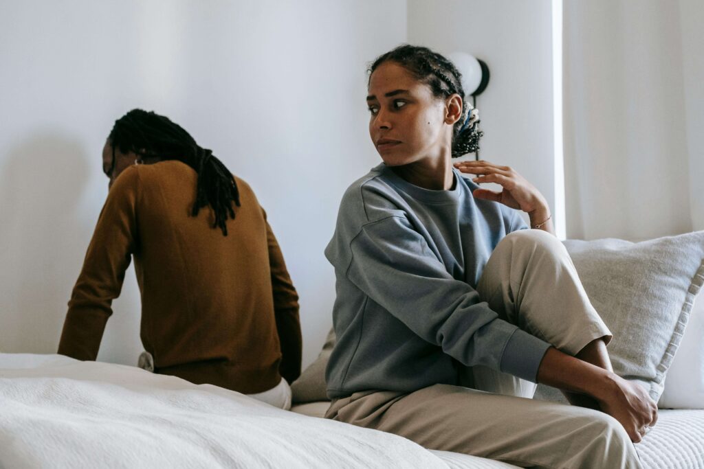 Emotional Distance - gottman couples therapy san diego ca - couples therapy san diego ca - couples counselor san diego ca - mission valley - la - san francisco - california Couple sitting on a bed together but looking distant, representing relationship challenges addressed through Gottman couples therapy in San Diego, CA.