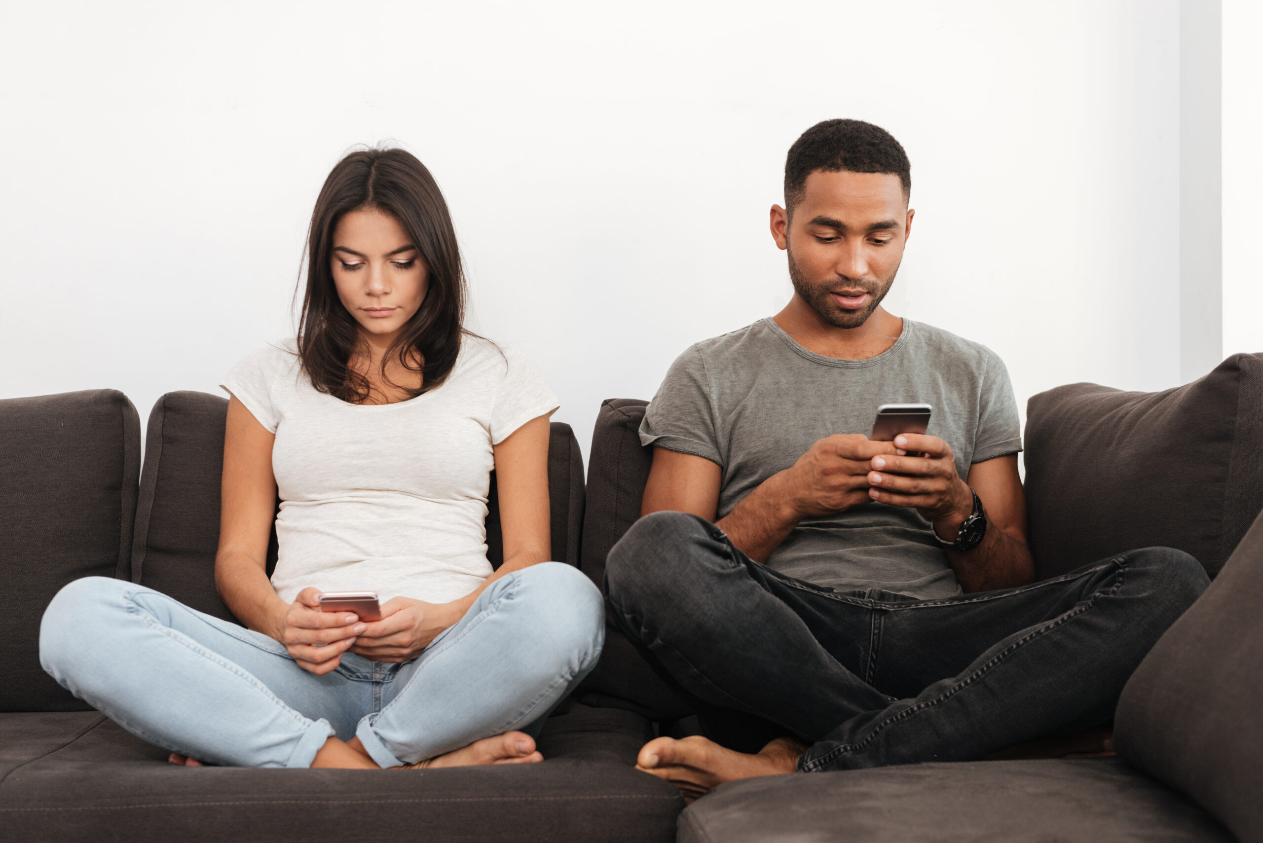Couple sitting apart and scrolling on phones—signs of disconnection and support from Gottman Couples Therapy on how to reconnect with your partner.