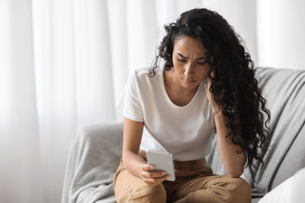 A worried woman looks at her phone, showing texting anxiety and the urge to stop overthinking in your relationship—Therapy for Anxiety & Relationships in San Diego, California with Stress Solutions.