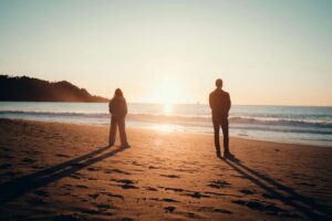 Wide shot of a couple standing apart on a beach with sunlight between them, representing transition and growth in couples therapy for conflict in San Diego, CA.