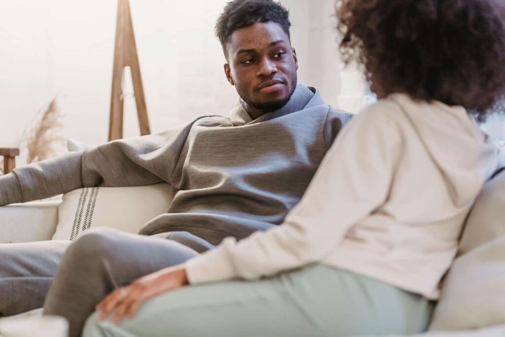 Couple sitting on a couch looking at each other contently, symbolizing openness and reconnection fostered through couples therapy for emotional avoidance in San Diego, CA.