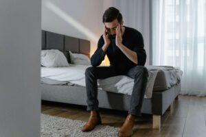 Man sitting on a bed looking stressed, representing emotional suppression explored in couples therapy for emotional avoidance in San Diego, CA.