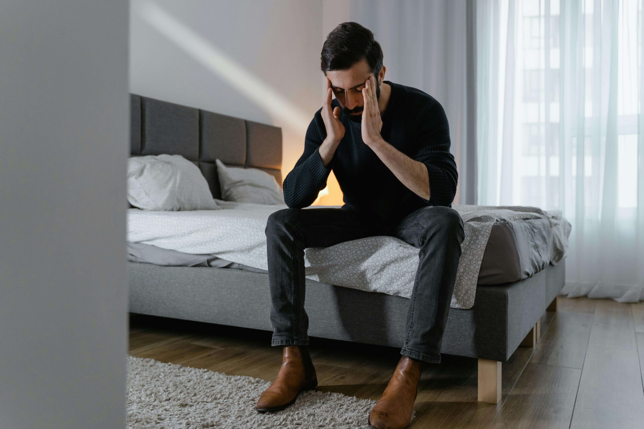 Man sitting on a bed looking stressed, representing emotional suppression explored in couples therapy for emotional avoidance in San Diego, CA.