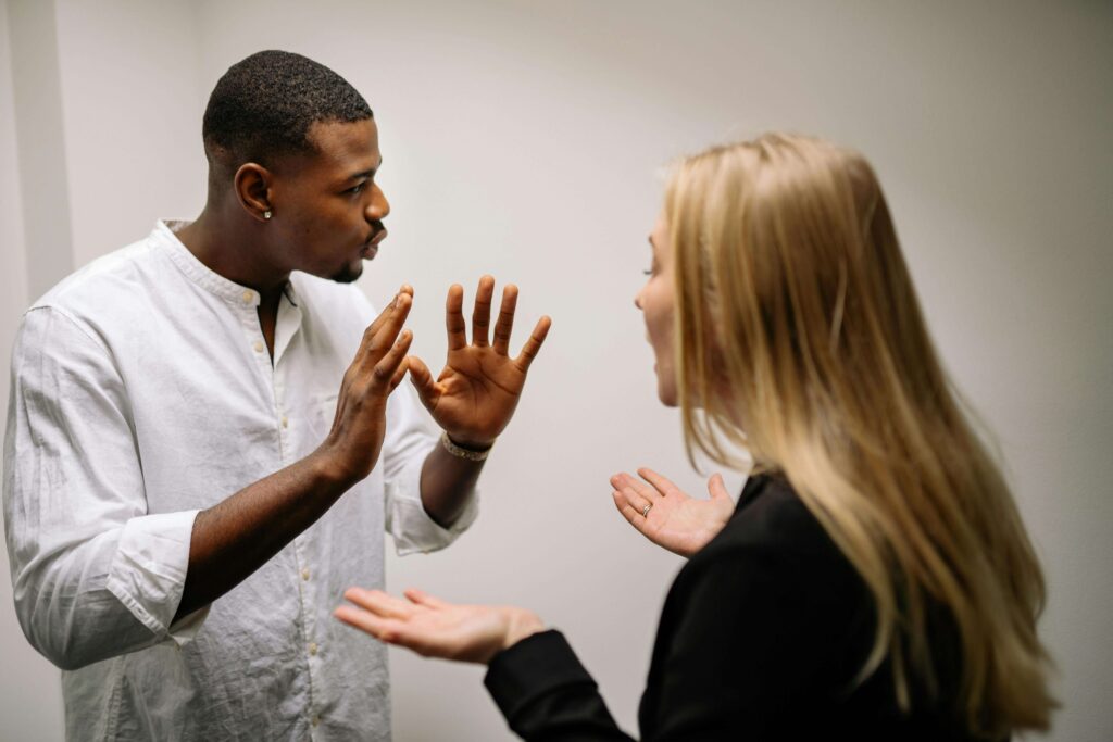 Couple arguing while the man holds his hands up in protest and the woman speaks, representing communication struggles addressed in couples therapy for defensiveness in San Diego, CA.