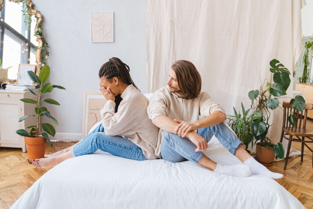 Relationship Frustrations - couples therapy san diego ca - couples counseling san diego ca - san diego couples therapy - mission valley - la - san francisco - california Couple sitting on a bed with the woman holding her face in her hands while her partner looks toward her, representing emotional struggles and the repair process supported through couples therapy in San Diego, CA.