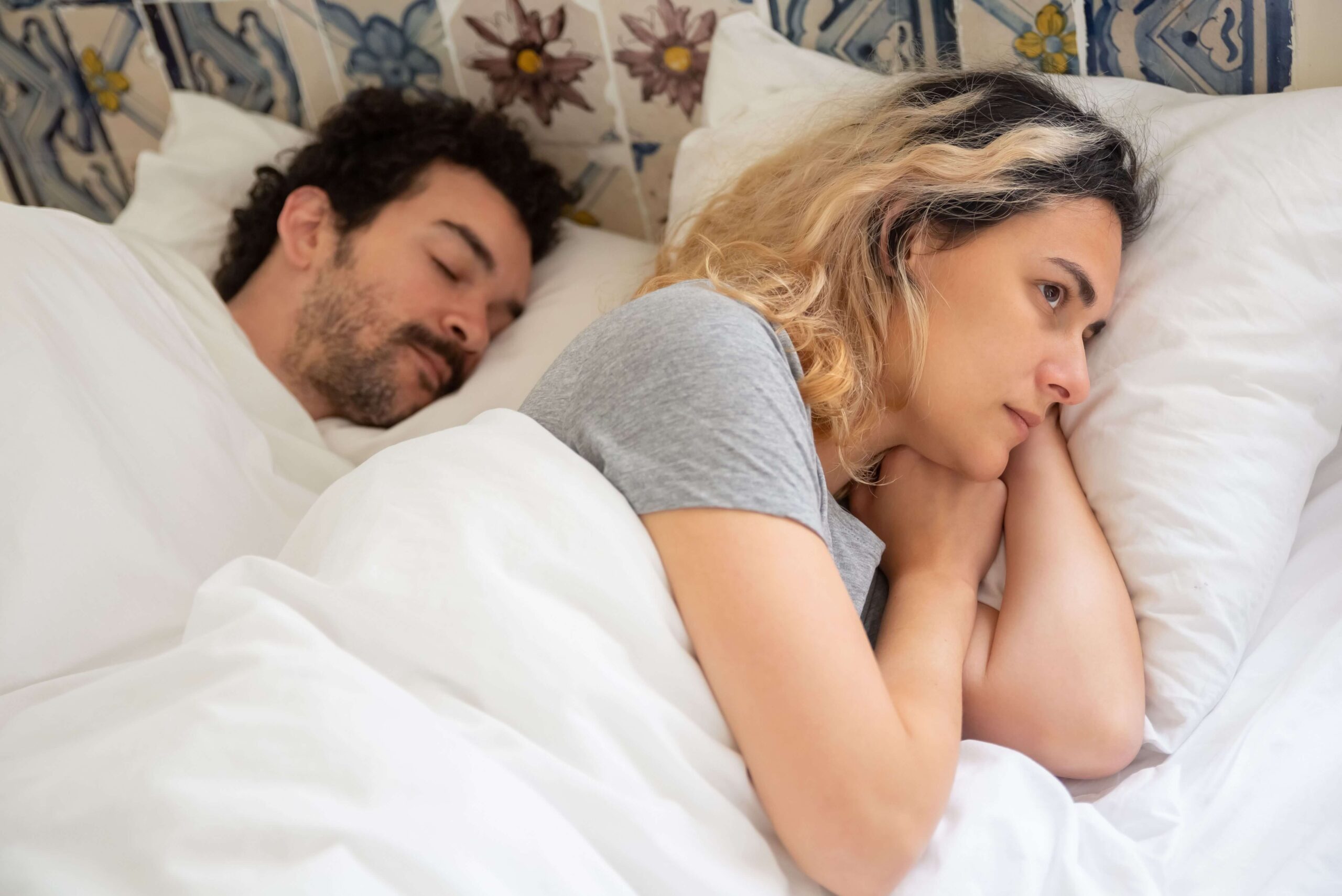 Couple lying in bed while appearing distant, representing relationship disconnection and communication challenges addressed through couples therapy in San Diego, CA.