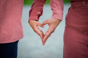 Close-up of a couple making a heart shape with their hands, representing love, connection, and attachment styles in San Diego, CA.
