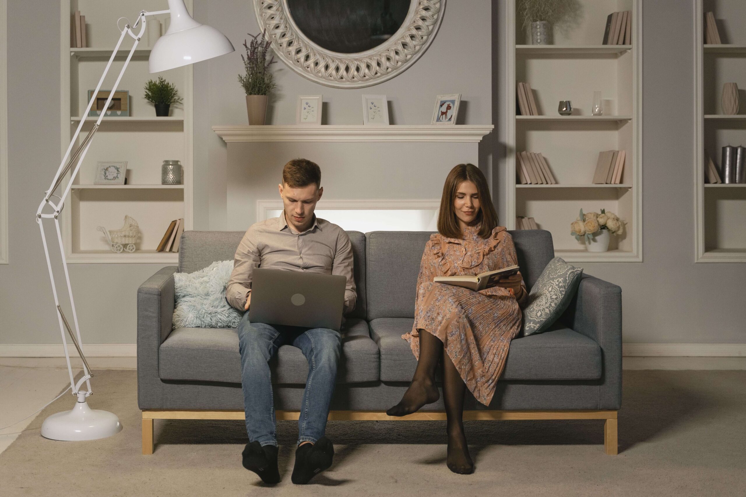 Couple sitting together on a couch while both appear distracted, representing disconnection and relationship challenges related to career stress addressed through couples therapy in San Diego, CA.
