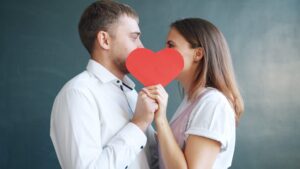 Couple holding a paper heart in front of their faces, representing affection, connection, and shared partnership supported through San Diego couples therapy.