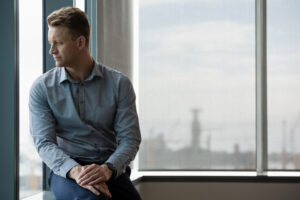 Thoughtful man sitting beside an office window, featured in an article about therapy for men in San Diego.